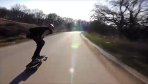 Un skater care coboara in viteza pe o sosea imbratiseaza din plin o masina care circula regulamentar